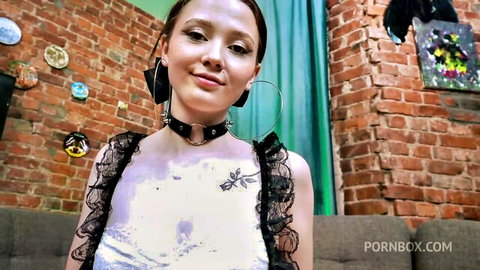 Petite teen with choker collar and sheer lace top smiling seductively on couch