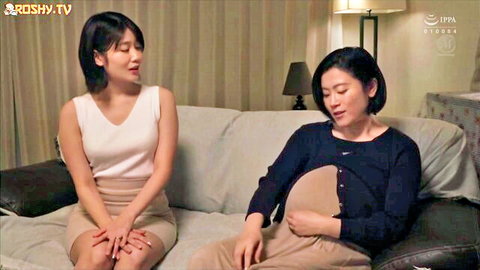 Young Asian brunette in tank top and skirt sits beside pregnant MILF on couch
