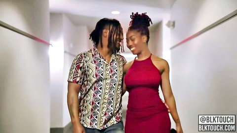 Sexy ebony babe in tight red dress embraced by dreadlocked black stud in hallway