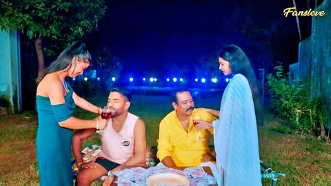 Indian women in dresses pouring wine for older men in outdoor group scene