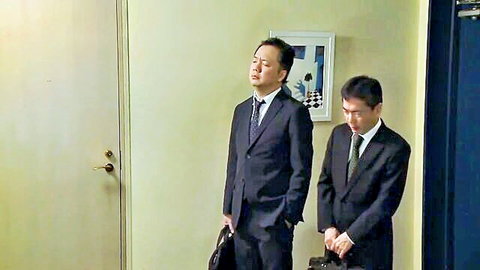 Two suited Japanese businessmen standing in office hallway discussing