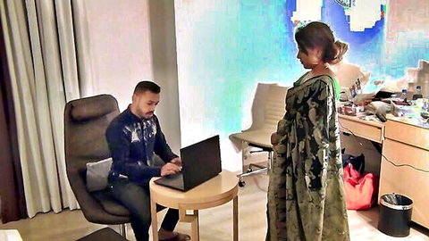 Indian woman in printed saree stands near bearded man working on laptop in office room