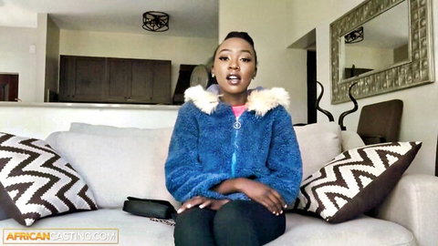Curvy ebony teen in fuzzy blue jacket, teasing expression on couch