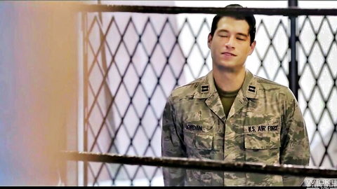 Handsome US Air Force soldier in camouflage uniform stands behind chain link fence