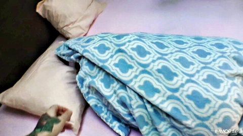 Tattooed hand gripping pillow on messy pink bed with blue blanket in amateur bedroom tease