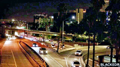 Nighttime aerial view of busy urban highway interchange with palm trees and city lights under Blackedraw watermark