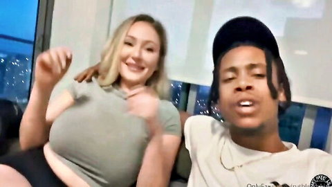 Busty blonde with huge tits smiles with black stud in cap on couch at night