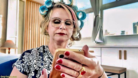 Blonde MILF in curlers and glasses seductively holds phone with red nails