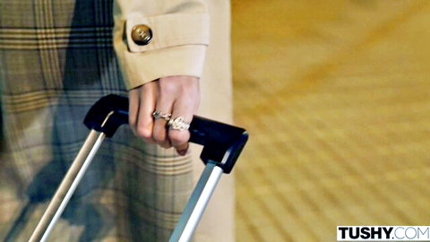 Bella Spark's elegant hand in trench coat holding suitcase, teasing travel vibe