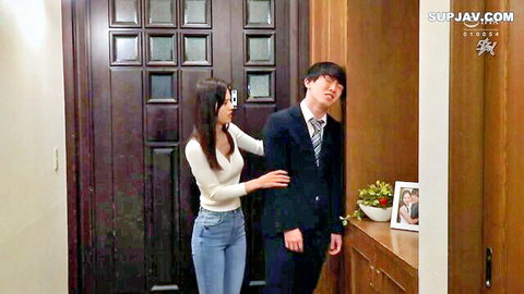 Brunette Japanese woman in tight white top and jeans touches suited East Asian man's shoulder in dim hallway