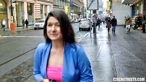 Brunette Czech woman in blue jacket and pink top walking on rainy urban street
