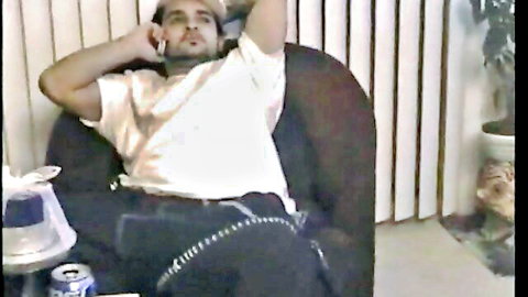 Sexy muscular man lounging in chair talking on phone with open shirt exposing chest