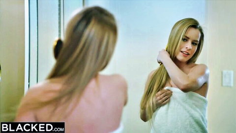 Blonde petite woman in white towel brushing long hair in mirror