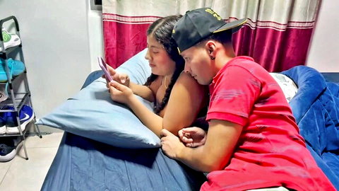 Latina stepsister in tight top cuddling with stepbrother on bed, watching phone intimately