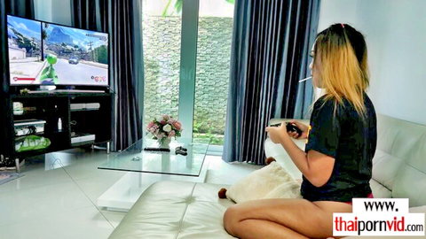Sexy blonde Thai gamer girl smoking cigarette while playing racing games on couch