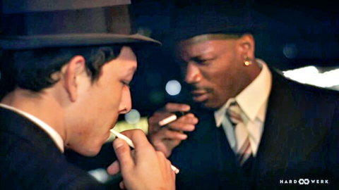 Two suited men in fedoras share a close smoke, interracial gay tease from Soiree Bang by HardWerk