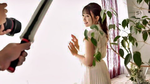 Asian woman in white pleated dress posing for photoshoot, smiling over shoulder