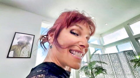 Syren De Mer smiling seductively with red hair in black top