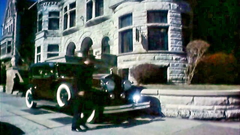 Vintage black limousine parked outside stone mansion at night with man in coat stepping out