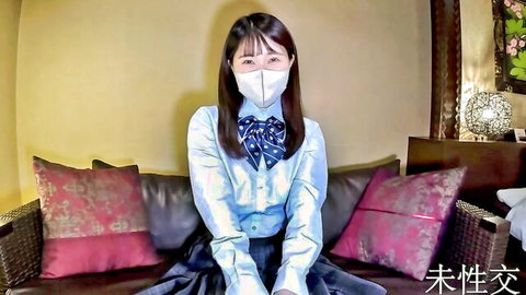 Japanese schoolgirl in uniform and mask sits teasingly on hotel bed with legs apart