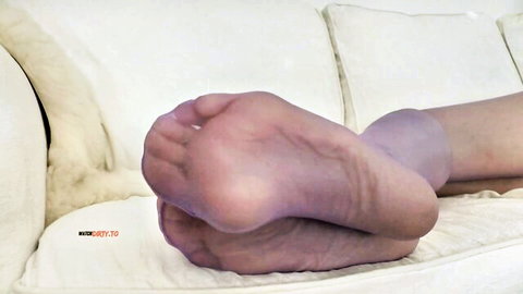 Close-up of sexy MILF's sheer pantyhose soles flexed toes spread on white couch