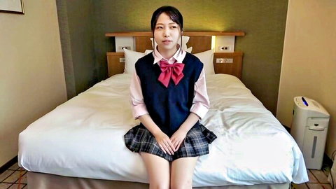 Cute petite Japanese teen in school uniform sitting on bed