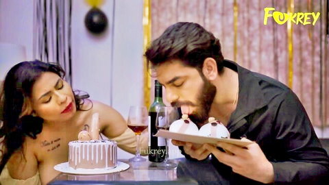 Topless Indian brunette with huge bare tits smiles topless at bearded man eating birthday cake at party