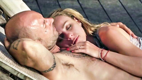 Blonde woman cuddles intimately with bald tattooed muscular man outdoors in French setting
