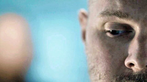 Intense close-up of bald bearded man with serious gaze, blue lighting