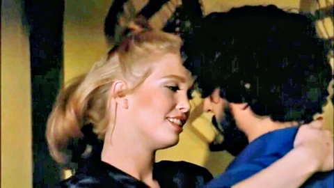Vintage blonde in black dress shares intimate embrace with bearded man in classic scene