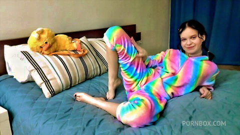 Smiling teen with pigtails pulls down rainbow onesie exposing perky tits on bed