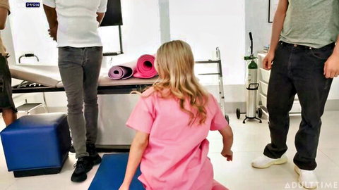Blonde nurse in pink scrubs squats teasingly surrounded by men in hospital room gangbang setup
