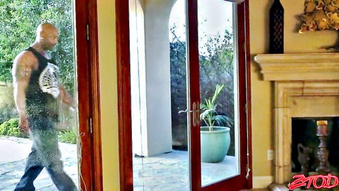 Muscular bald black bull in wet tank top walks through glass doors into luxurious room