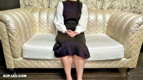 Petite Japanese teen in black dress with white sleeves sitting demurely on tufted couch