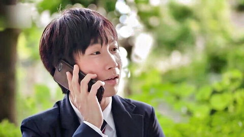 Asian man in suit talking on flip phone outdoors in green park