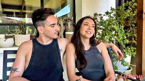 Smiling brunette in tank top sits close with tattooed guy on outdoor patio