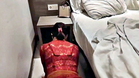 Indonesian brunette in red dress kneels by hotel bed arching big ass teasingly