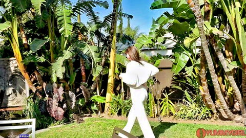 Sexy brunette walking away in tropical garden wearing tight white outfit teasing her ass