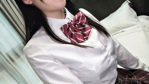 Sexy Japanese schoolgirl in tight white blouse and red bowtie teasing on bed