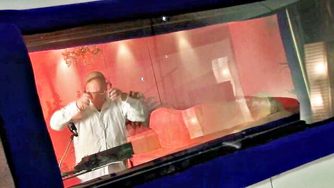 Intense man in white shirt sings passionately into mic wearing headphones in red-lit recording booth
