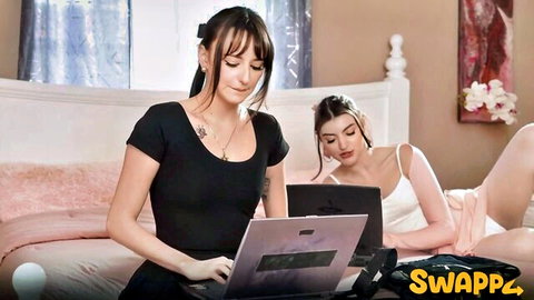 Two sexy young brunettes in lingerie tops typing on laptops teasing on bed