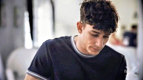 Handsome curly-haired young man in navy shirt with white trim looks intensely indoors