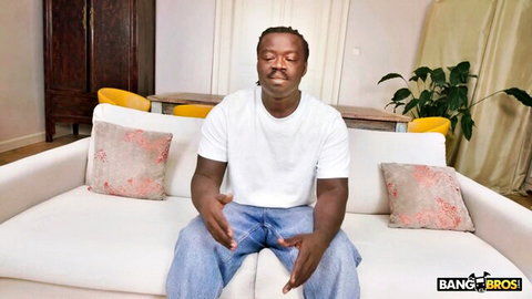 Black man in white tee and jeans sits relaxed, Bang Bros anal scene with Miami