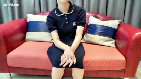 Japanese employee in tight navy sailor uniform sits primly on red leather couch teasing