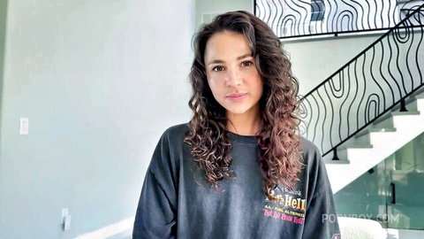 Skinny young brunette with small tits and long wavy hair smiling teasingly in POVBoy t-shirt