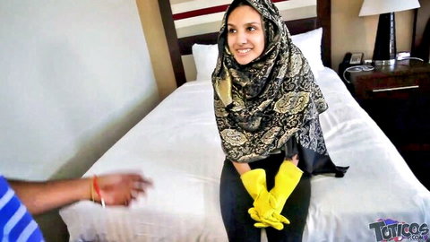 Jasmine Angel in hijab and yellow gloves, smiling on bed