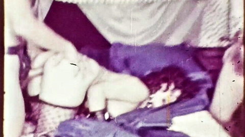 Vintage brunette with curly hair lying on purple pillows covered in white sheets teasing big tits