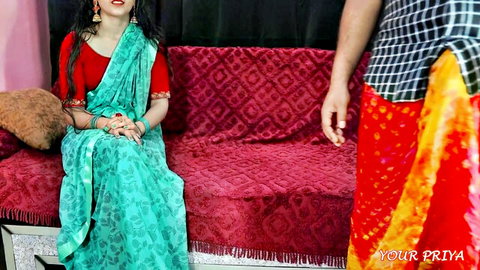 Sexy Indian brunette Priya in sheer green saree and red blouse smiling seductively on red couch with man in dhoti