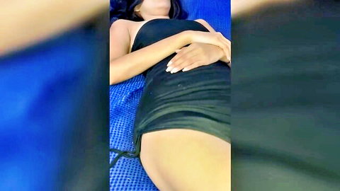 Seductive Asian teen in black dress lying on lounge, teasing pose