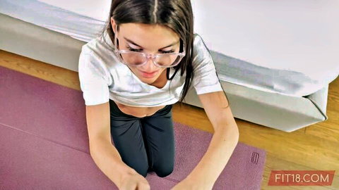 Fit teen with glasses kneels on yoga mat in tight white top and leggings teasing her curves